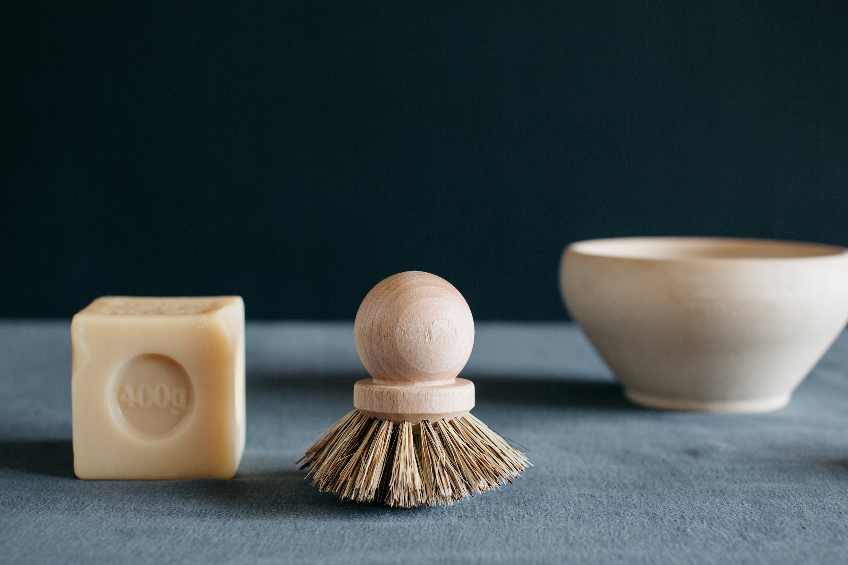 Cube of marseille soap next to wooden dish brush and bowl.