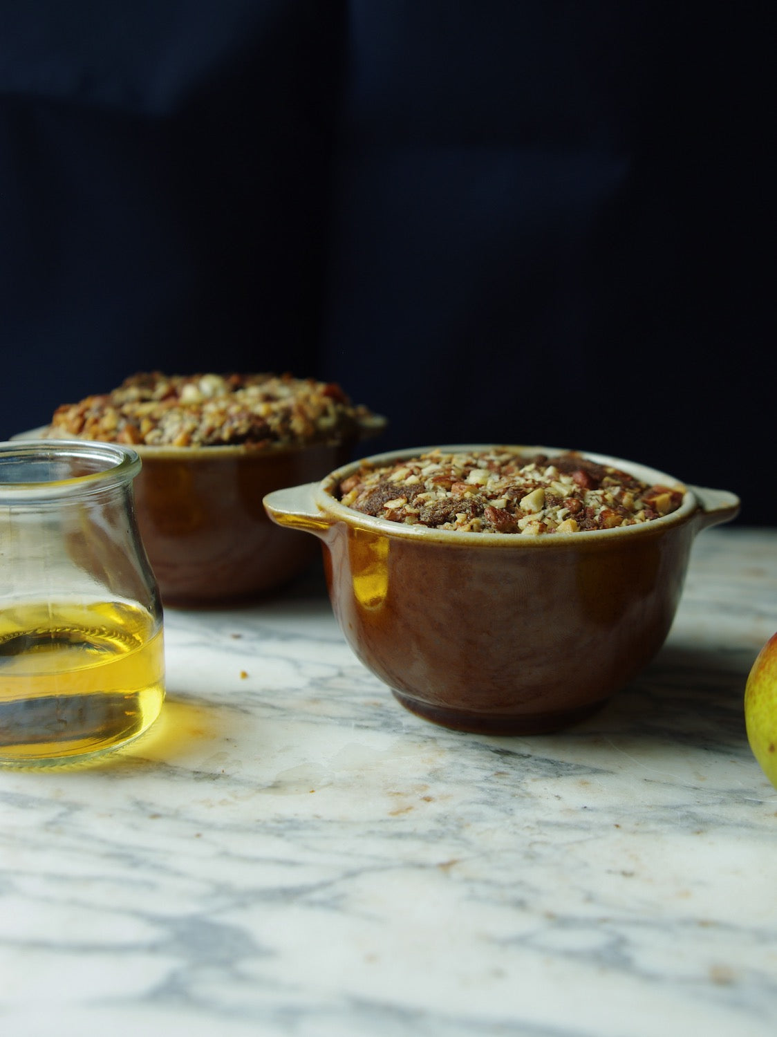Two brown handled bowls holding baked nut bread on marble counter next to small glass jar.
