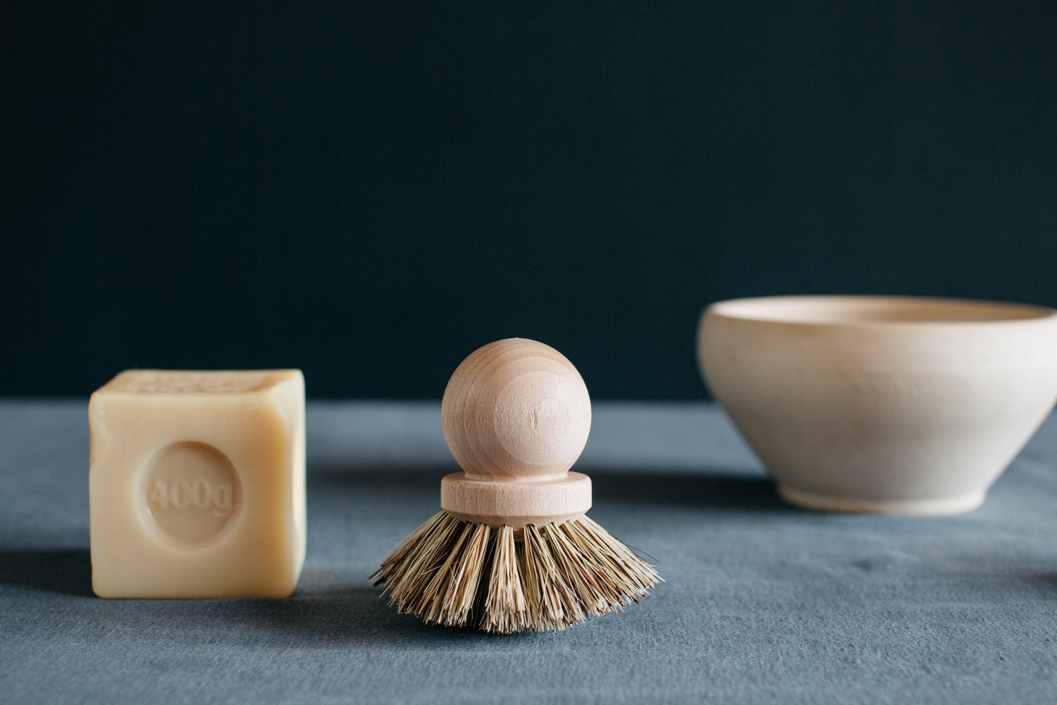Cube of marseille soap next to wooden dish brush and bowl.