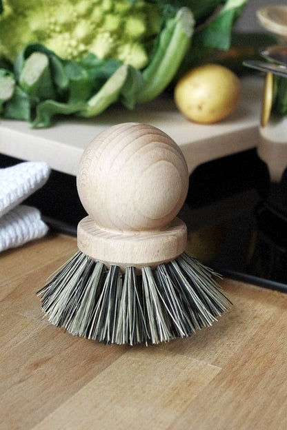 Natural wooden scrub brush with natural bristles on wooden countertop surrounded by vegetables.