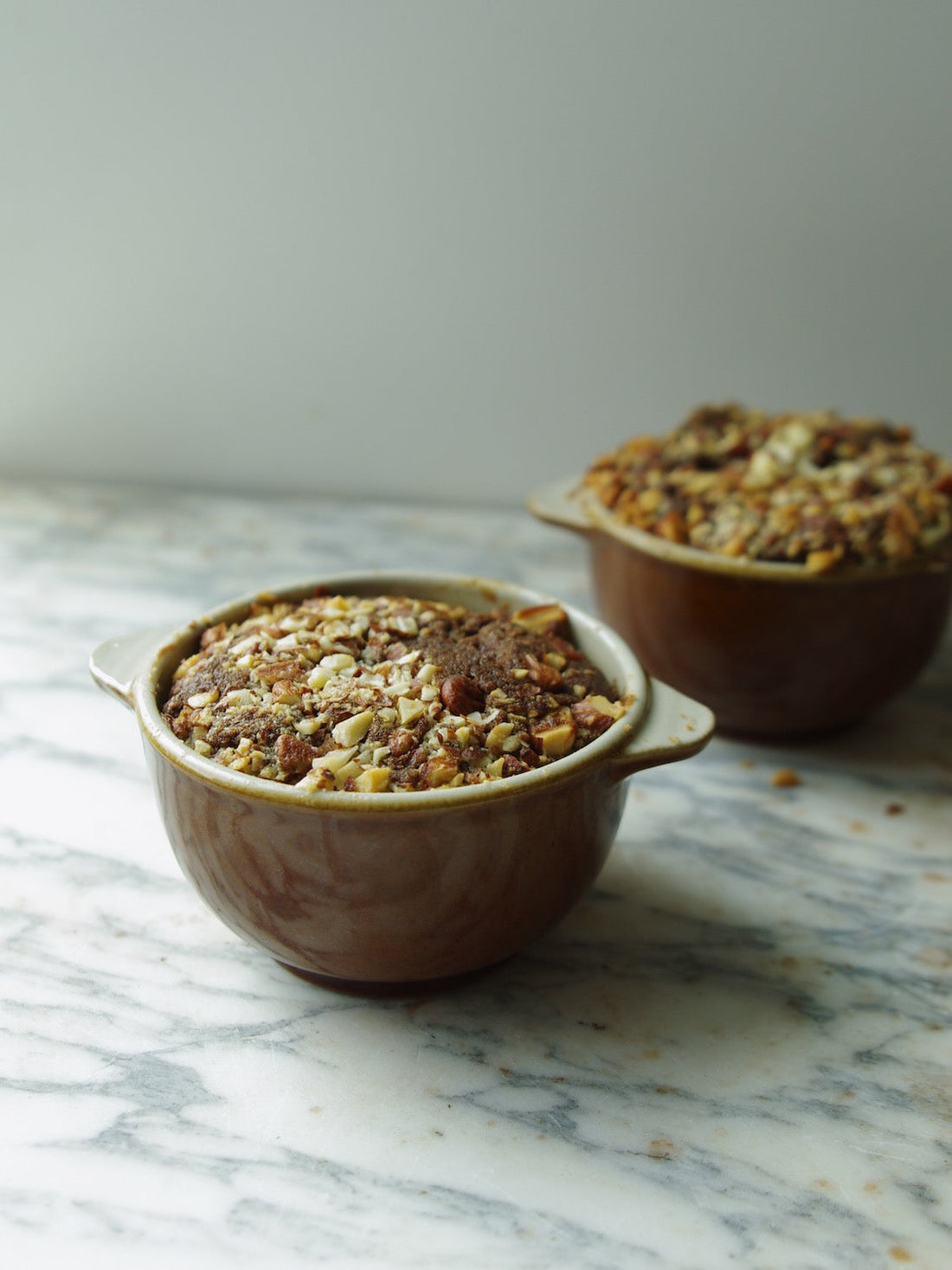 Two brown handled bowls on a marble counter holding a baked nut bread.